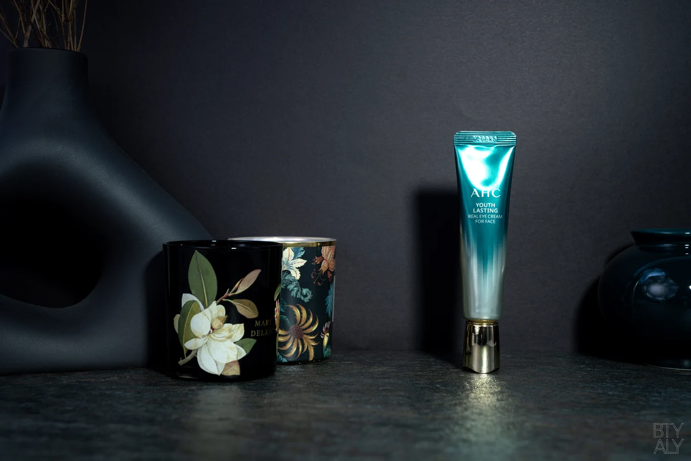 AHC Youth Lasting eye cream styled with candles against a dark, premium backdrop