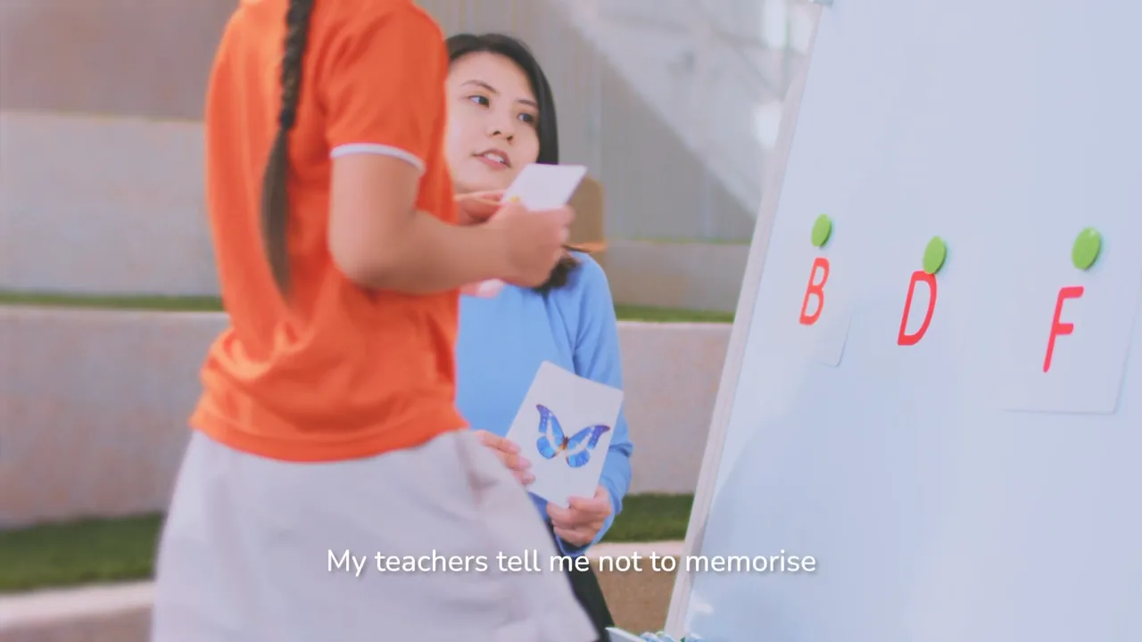 A My First Skool teacher with a girl at a whiteboard of letters, from the campaign film