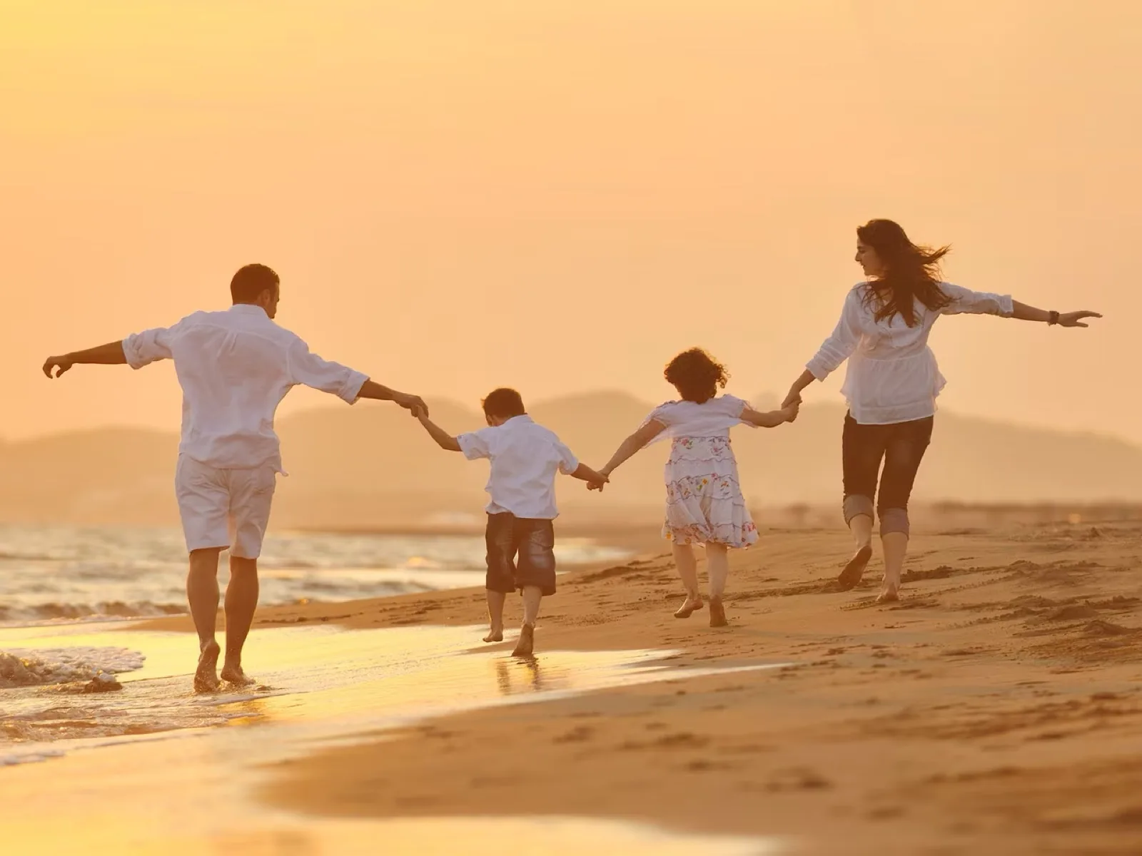 A family running hand in hand along a beach at sunset, Emirates Skywards My Family